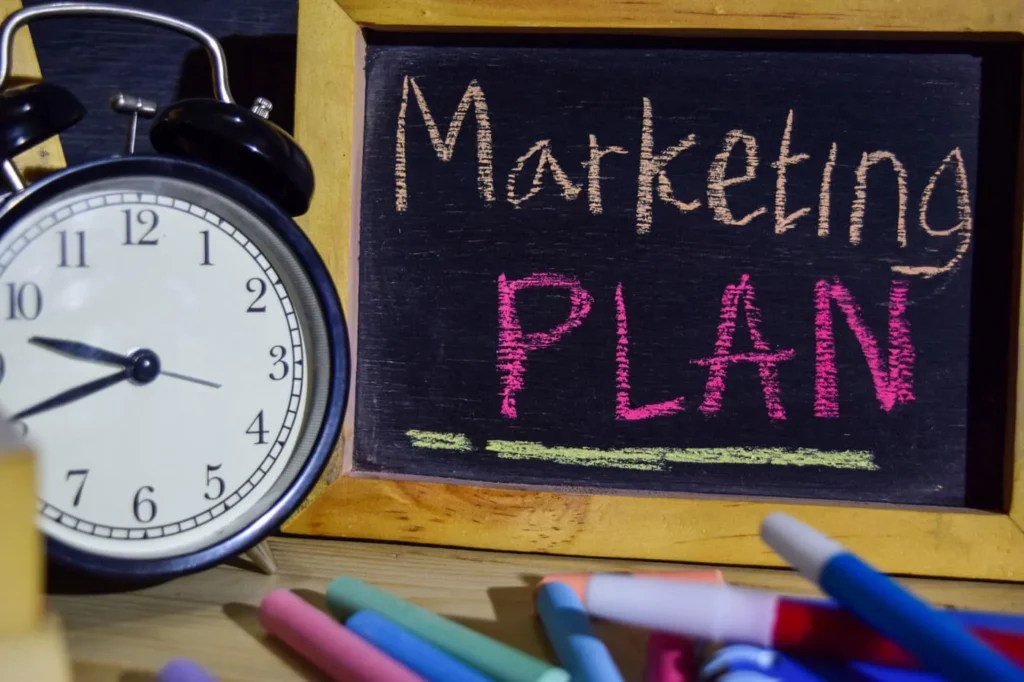 Ristrutturare il Piano di Marketing immagine composta con una grande sveglia in primo piano e una lavagna sullo sfondo